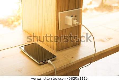 Mobile phone charging plugged on  wooden pole in the coffee shop with sunlight in morning time.