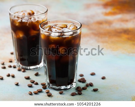 Ice coffee in a tall glass with cream poured over and coffee beans. Cold summer drink on a blue rusty background with copy space