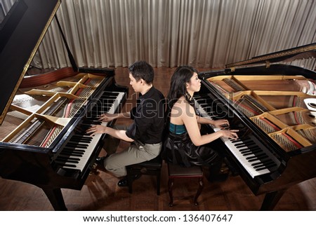 Two people, a couple playing duet musical performance with two grand pianos