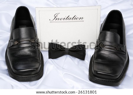 Card with \'invitation\' word printed on it and placed between man shoes and bow tie placed in front of it.