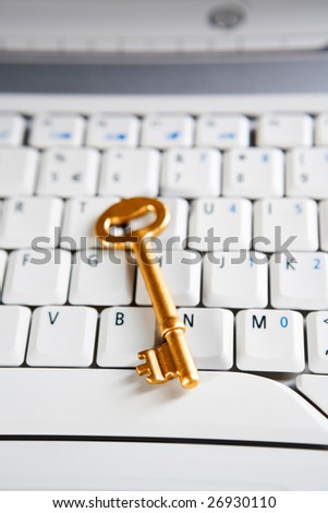 A golden key placed on the keyboard of a laptop. Very shallow depth of field, focus mainly on the tip of the key.