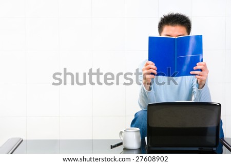 Man reading manual book in front of his laptop