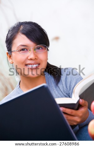 A young Asian scholar woman smiling to camera while holding book
