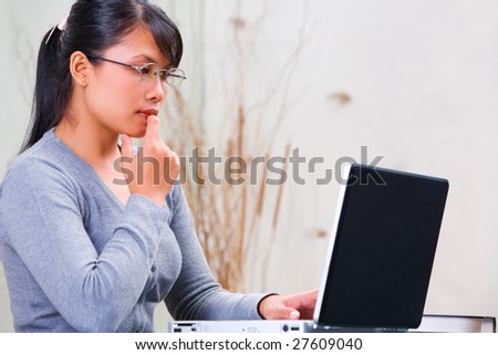 Young Asian woman thinking in front of her laptop
