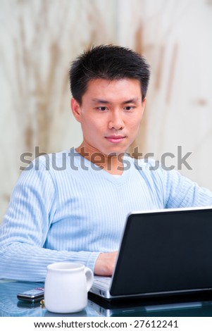 Portrait of young Chinese man using laptop for browsing internet at home.