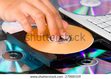Fingers pressing the DVD on DVD-ROM tray of a laptop.