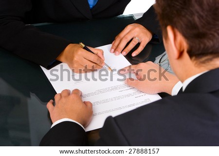 A business man is pointing a place where she should sign the agreement.
