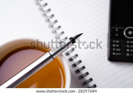 Placing a fountain pen on the coffee cup with book and mobile phone blurred in background