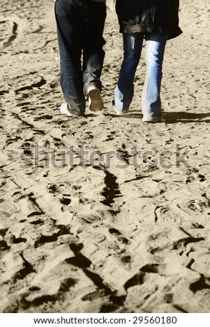 A couple walking together on sand toward their destination. Blur on foot movement is visible.