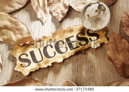 Global success concept made from word success printed on burnt paper and a glass globe with dry leaves scattered around, and using hard lighting