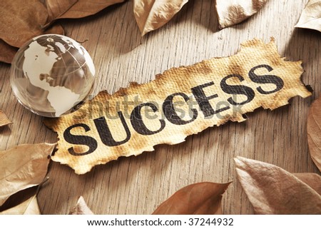 Global success concept using printed word on burnt paper along with compass and golden key, surrounded by dry leaf