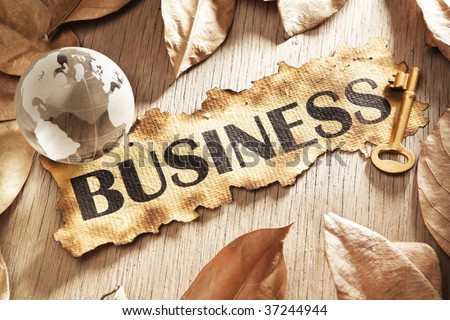 Key to global business concept using printed word on burnt paper along with galss globe and golden key, surrounded by dry leaf