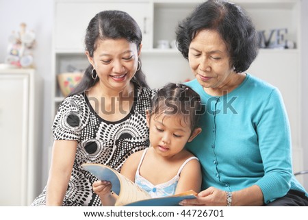 Little Asian girl accompanied by her mother and grandma reading book