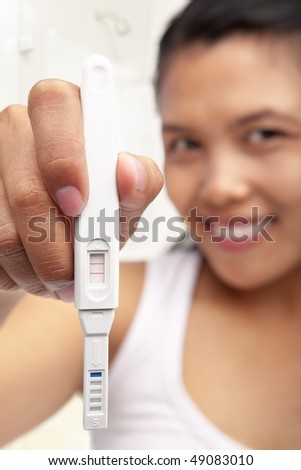 A happy Asian woman holding pregnancy test with positive result
