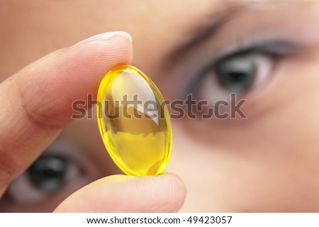A woman holding a yellow vitamin capsule, close up