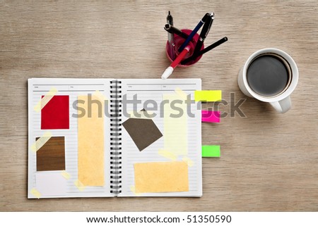 Designer scrap book, filled with various paper and material on wooden table, placed with mug of coffee and pen holder