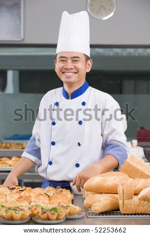 Asian chef or baker posing in front of the pastries in the commercial kitchen