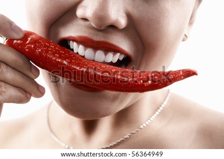 Woman holding big red chili in front of her mouth, about to bite or eat it