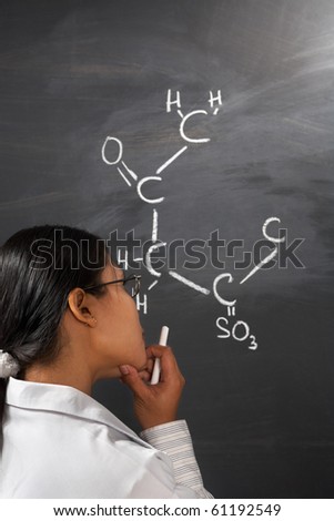 Female student thinking hard about chemistry problem on blackboard