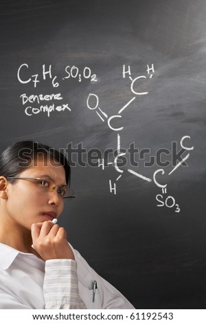 Female student thinking hard about chemistry problem on blackboard