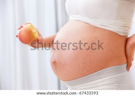 Unrecognizable pregnant lady holding an apple beside her big stomach
