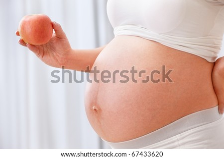 Unrecognizable pregnant lady holding an apple beside her big stomach