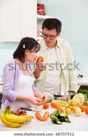 Asian couple ( pregnant wife ) busy preparing food in kitchen