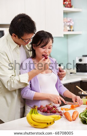 Asian couple activity in kitchen, with lots of fruit and vegeteable, where the couple eating fruit