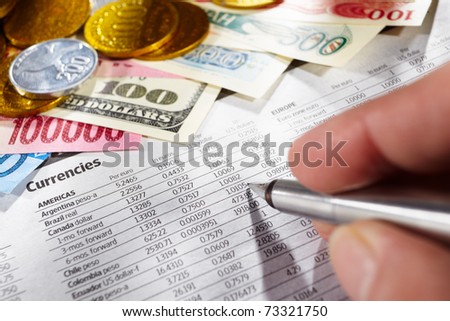 Hand on pen observing the foreign exchange data with money from different countries on edge