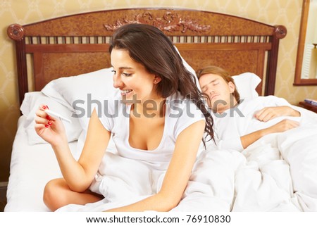 Lady looking at the pregnancy test device on bed while her spouse still sleeping