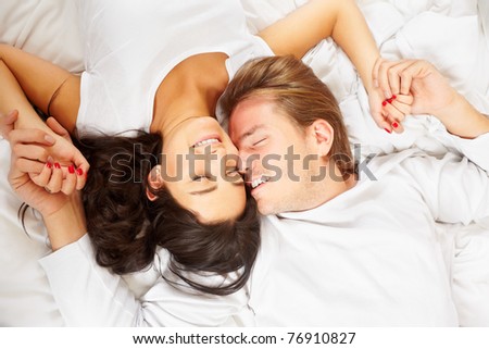 A happy romantic couple pose on white covered bed, showing their love for each other
