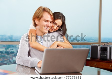 Lady hug her spouse from behind looking very happy in front of the laptop