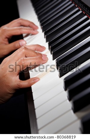 Hand playing on piano keys, using spot lighting