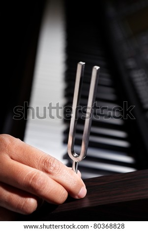 Hand holding tuning fork on top of piano wood panel
