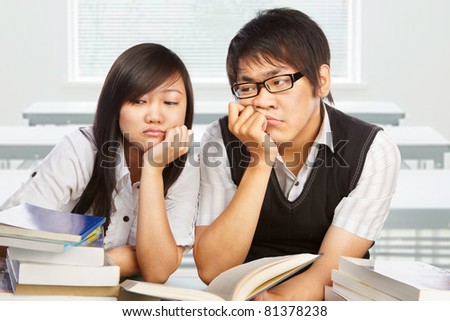 Two stressful students looking away to the books in the classroom