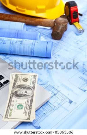 Cash over laptop and other working tools with blueprint of residential design on the bottom