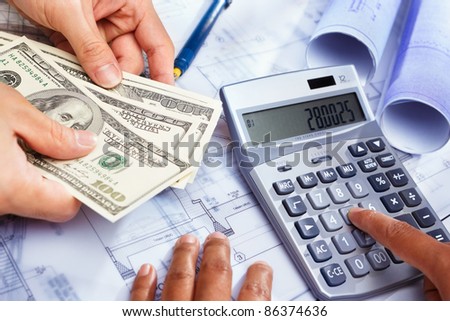 Hand calculating the cost of house construction, with blue print  on bottom