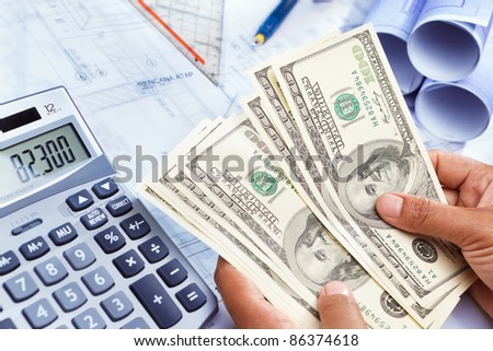 Hand counting the money for cost of house construction, with blue print  on bottom