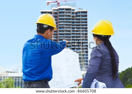 Two contractors, man and woman facing the building project in progress