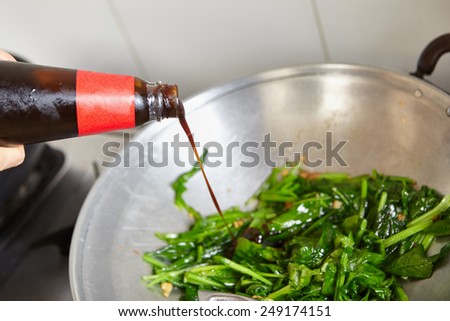 Pouring sauce to the vegetable on the wok. Main focus on the poured sauce liquid near the tip of the bottle, very shallow one