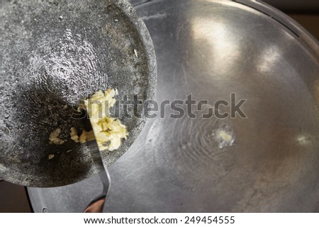 Add the crushed garlic to the wok filled with hot cooking oil. movement blur noticeable by spatula push the garlic from stone mortar.