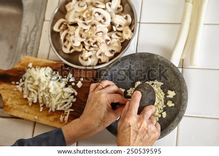 Hand crushing the garlic on mortar, slight movement blur on hand holding pebble to crush it.