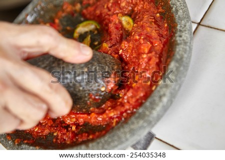 Making sambal, special chili food in Indonesia to eat together with another meal to add hot and spice flavor, all the ingredient crushed using stone pestle on stone mortar