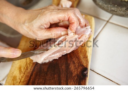 Hand cutting chicken breast on cutting board