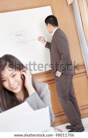 Chinese businesswoman on the phone while businessman preparing presentation on background