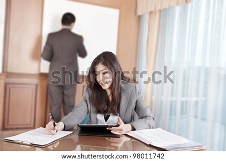 Chinese businesswoman busy working with her tablet while businessman on background busy preparing presentation