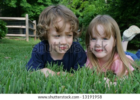 2 children laying in the grass. \'Mom says we need to sit here and smile\'