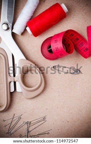 Tools for sewing and handmade: thread, scissors, pins on brown paper.
