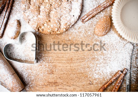 Christmas and holiday baking background, flour, bakeware, heart, cinnamon, cookies and almonds on a wooden board, viewed from above