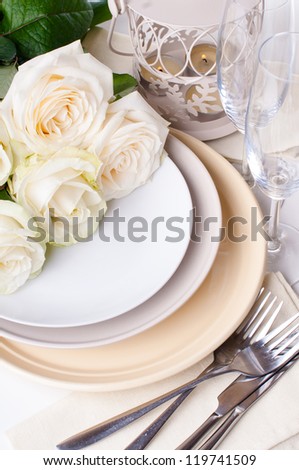 Festive table setting with beige roses, wine glasses, candles, napkins and cutlery